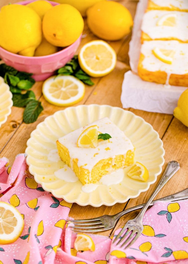 A square slice of lemon sheet cake on a pink napkin on a wooden table.