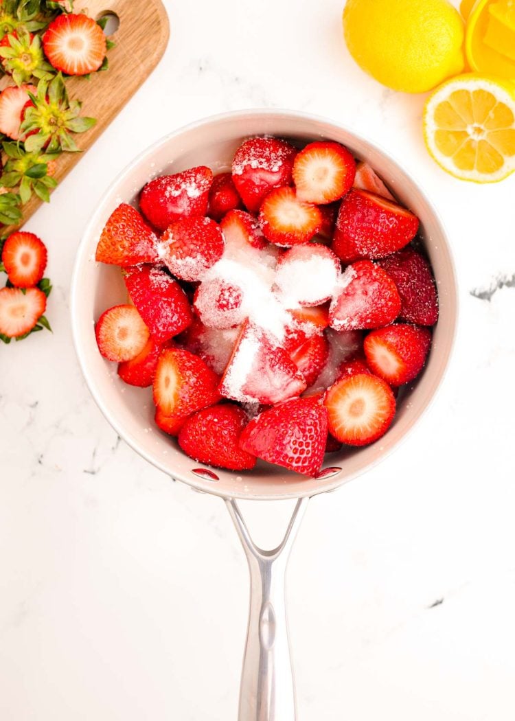 Strawberries, sugar, and lemon juice on a white marble counter.