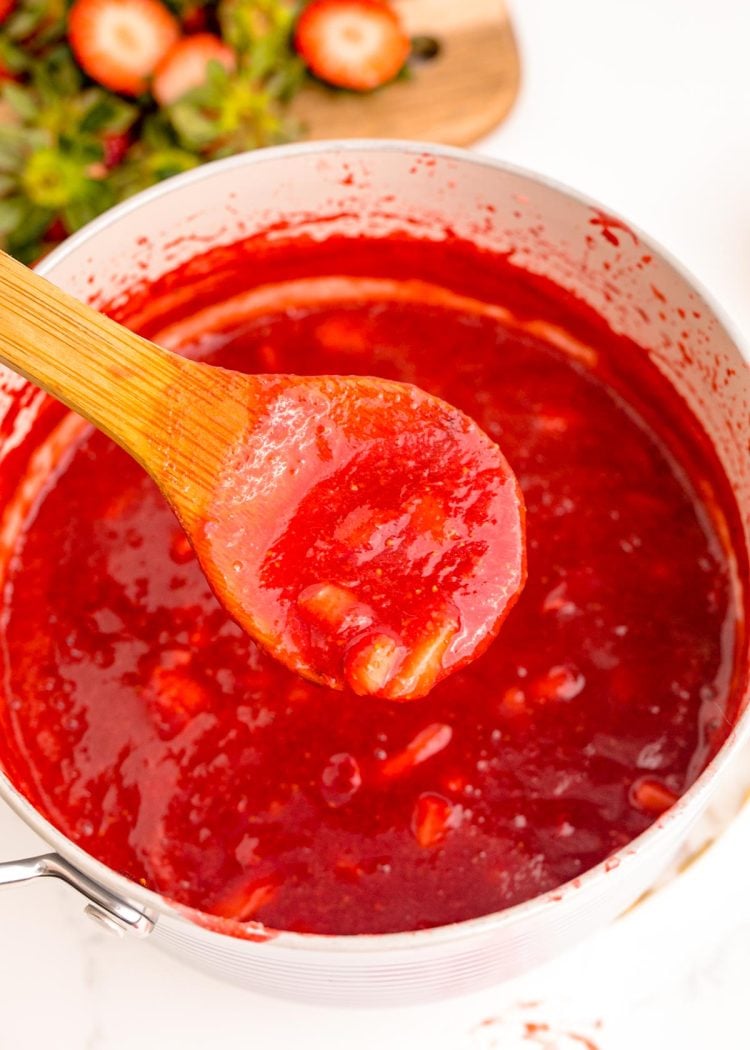 A wooden spoon scooping strawberry puree out of a pot.