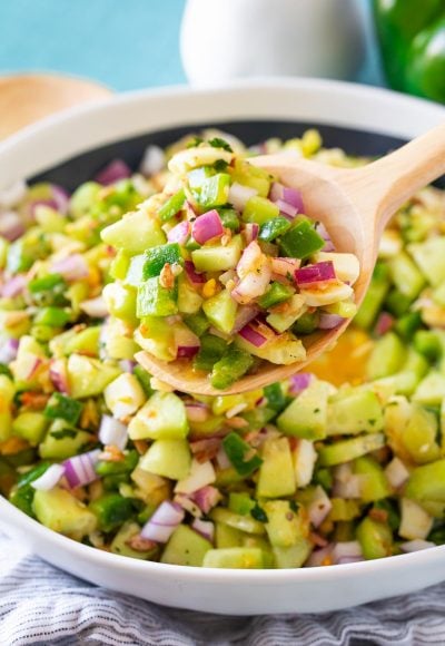 A serving spoon scooping cucumber salad out of a white serving bowl.