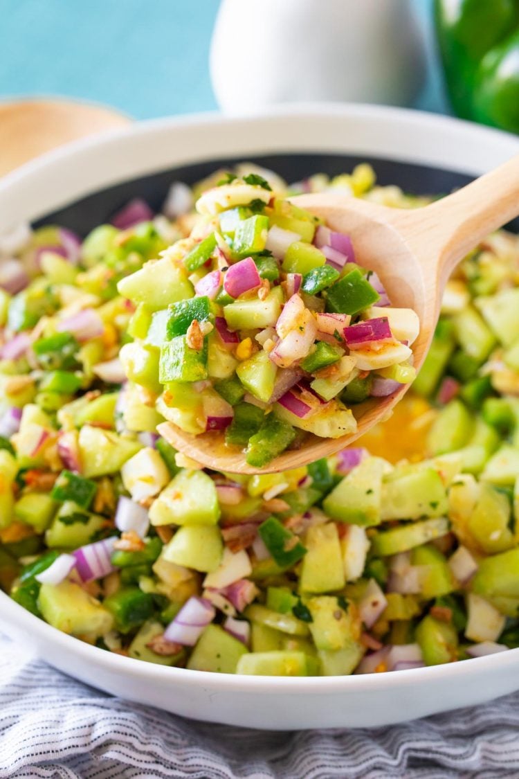 A serving spoon scooping cucumber salad out of a white serving bowl.