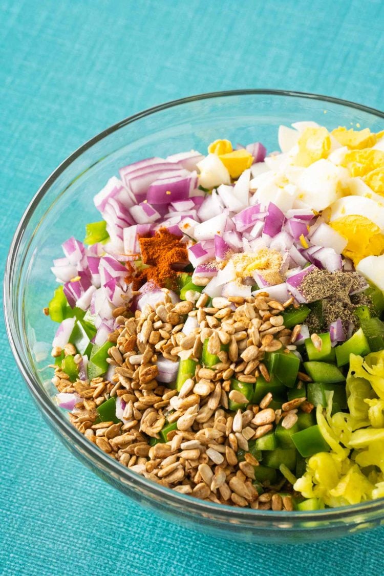 Ingredients for hot girl summer salad in a glass mixing bowl on a blue surface.