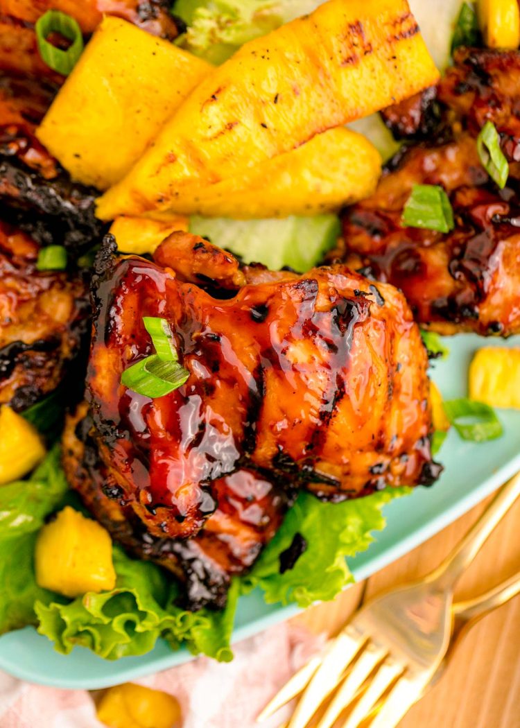 Close up of a piece of grilled huli huli chicken on lettuce with pineapple.