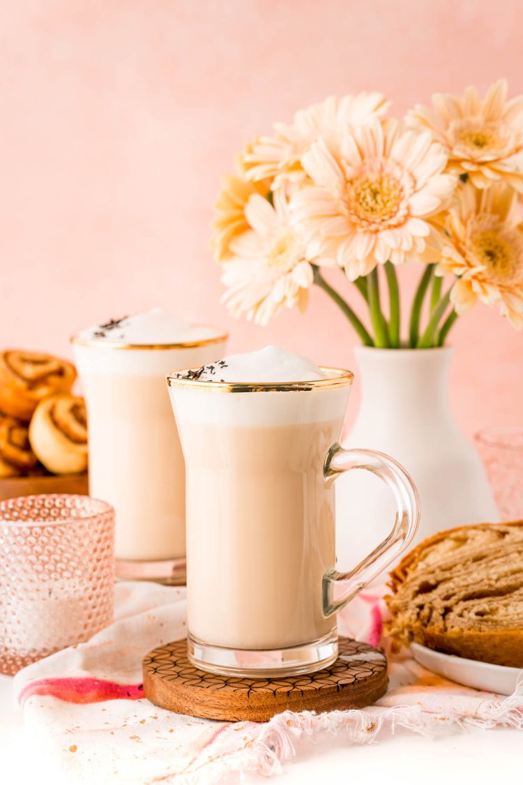 Close up of a london fog latte in a glass mug with flowers in the background.