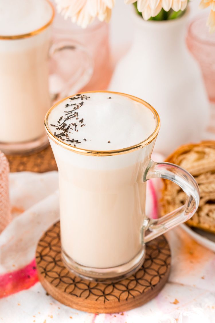 Close up of a london fog latte in a glass mug with flowers in the background.