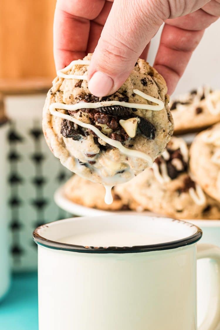 A woman's hand dipping an Oreo Chocolate Chip Cookie in a mug of milk.