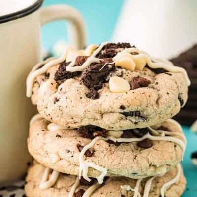 Chocolate chip oreo cookies stacked against a mug on a blue surface.