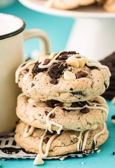 Chocolate chip oreo cookies stacked against a mug on a blue surface.