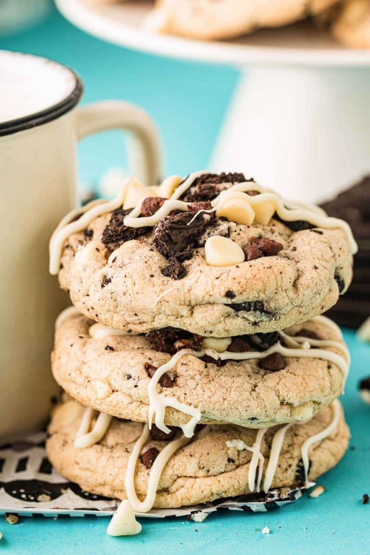 Chocolate chip oreo cookies stacked against a mug on a blue surface.