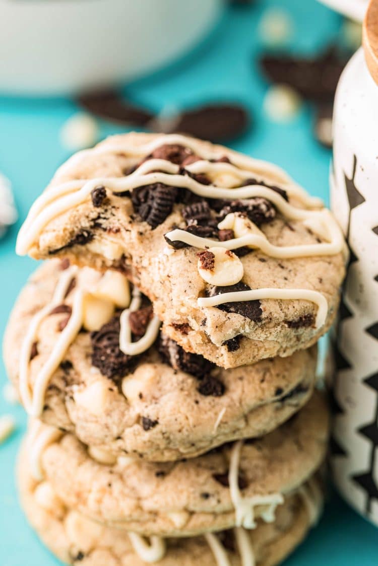 A stack of oreo chocolate chip cookies leaning against a mug with the top one missing a bite.