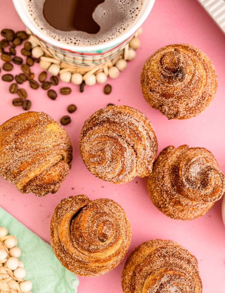 Overhead photo of cruffins on a pink surface with a mug of coffee.