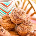 Cruffins stacked on a wooden cutting board with a mug of coffee in the background.