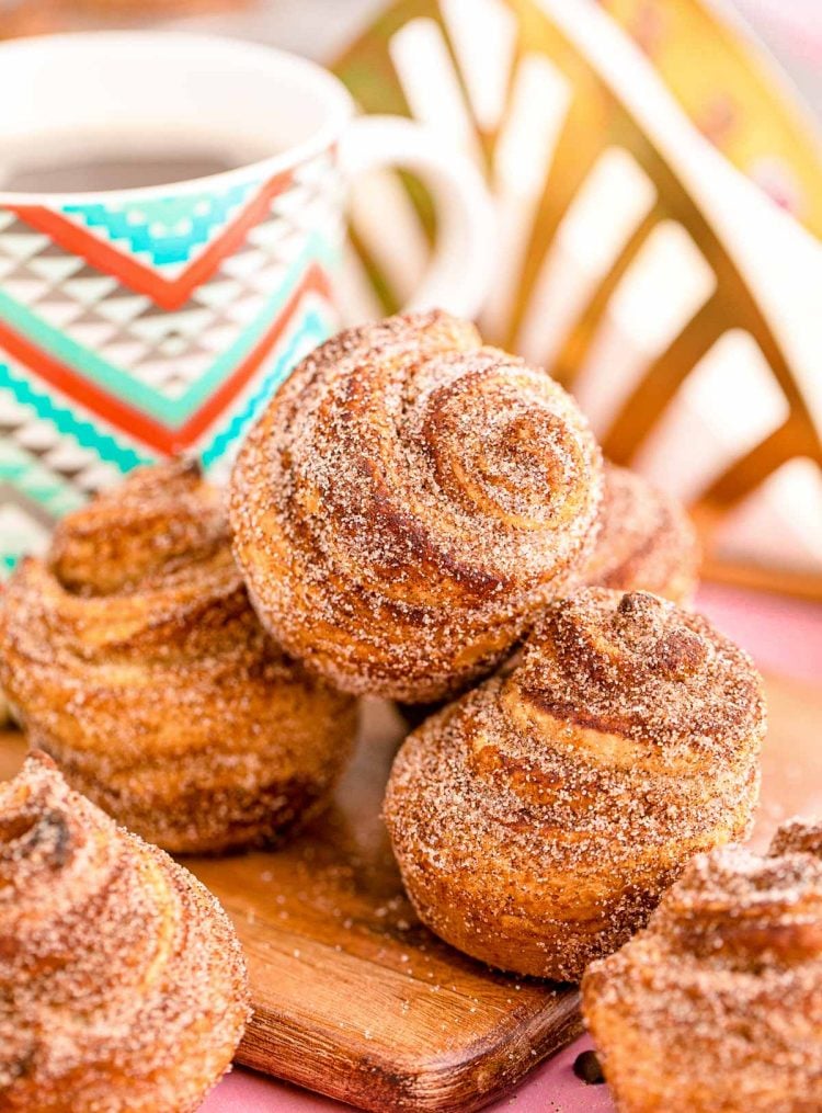 Cruffins stacked on a wooden cutting board with a mug of coffee in the background.