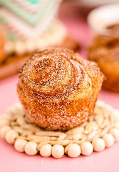 Close up photo of a cruffin sitting on a coaster on a pink surface.