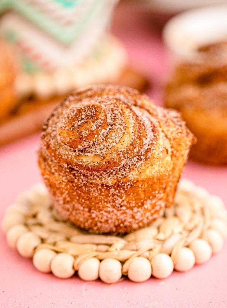 Close up photo of a cruffin sitting on a coaster on a pink surface.