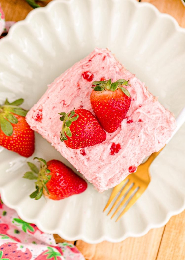 Overhead photo of strawberry sheet cake on a white scalloped plate.