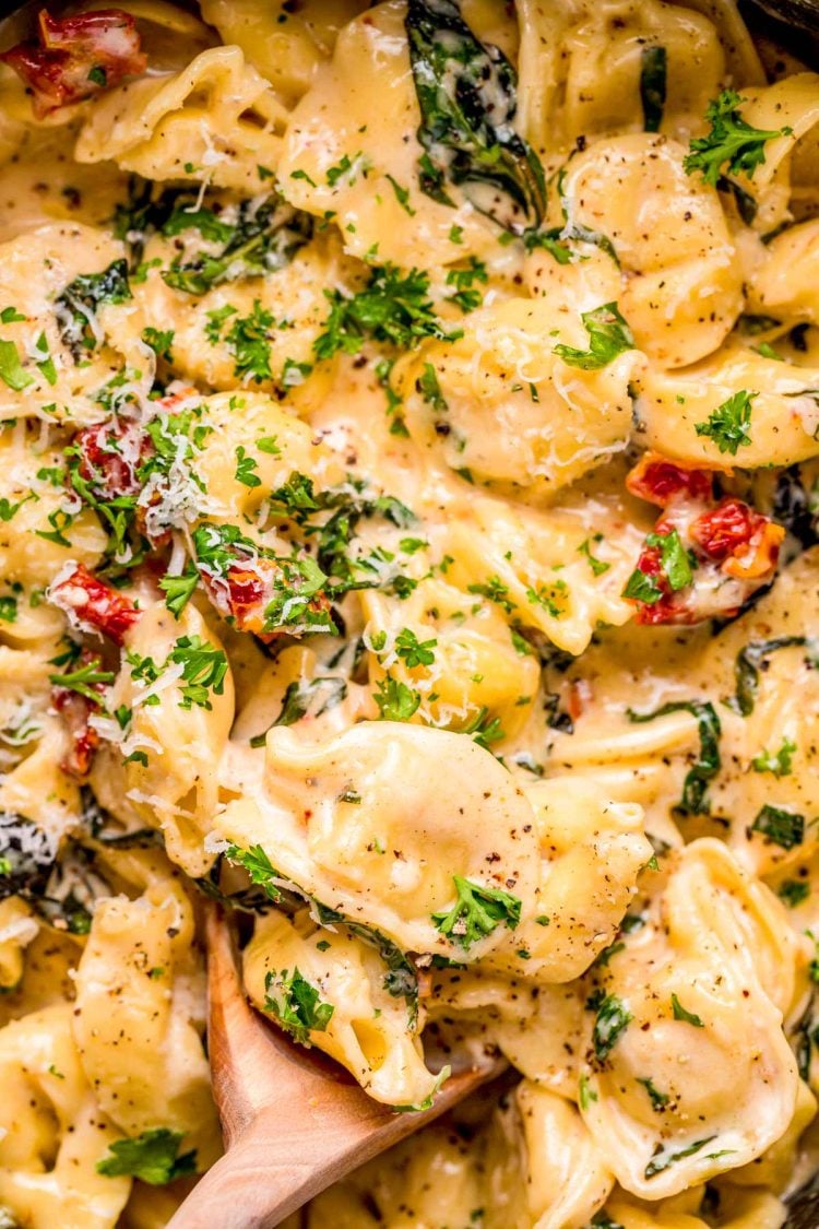 Close up photo of a wooden spoon in a pot of tortellini alla panna.