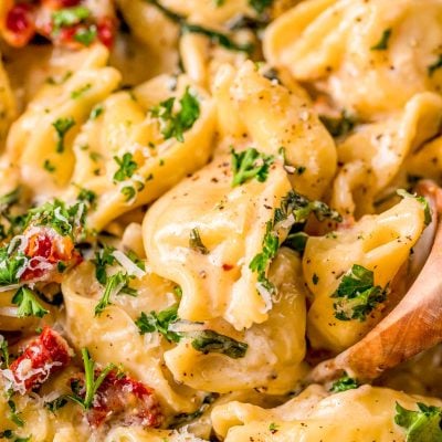 Close up photo of a wooden spoon in a pot of tortellini alla panna.