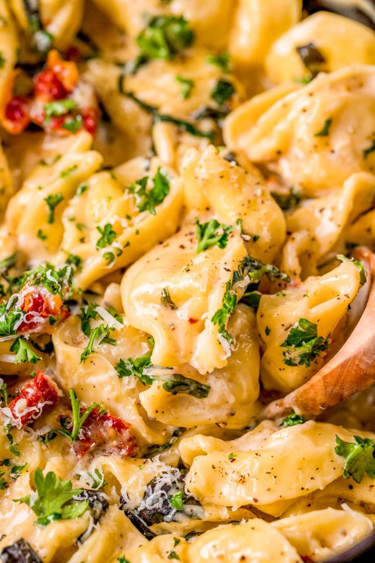 Close up photo of a wooden spoon in a pot of tortellini alla panna.