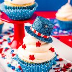 Close up photo of a 4th of July cupcakes decorated with a mini blue top hat and red star sprinkles.