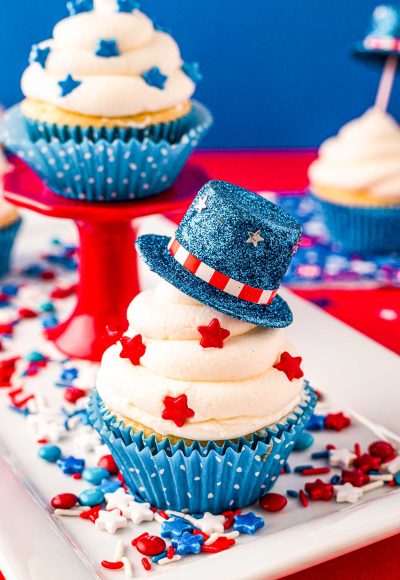 Close up photo of a 4th of July cupcakes decorated with a mini blue top hat and red star sprinkles.