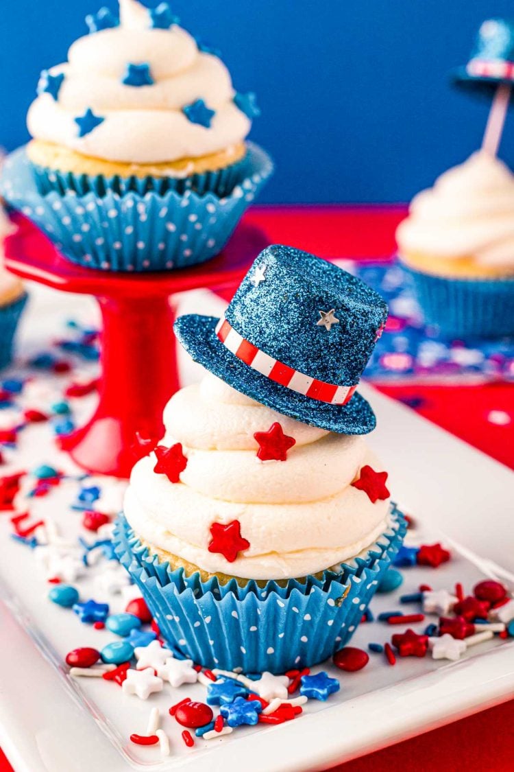 Close up photo of a 4th of July cupcakes decorated with a mini blue top hat and red star sprinkles.