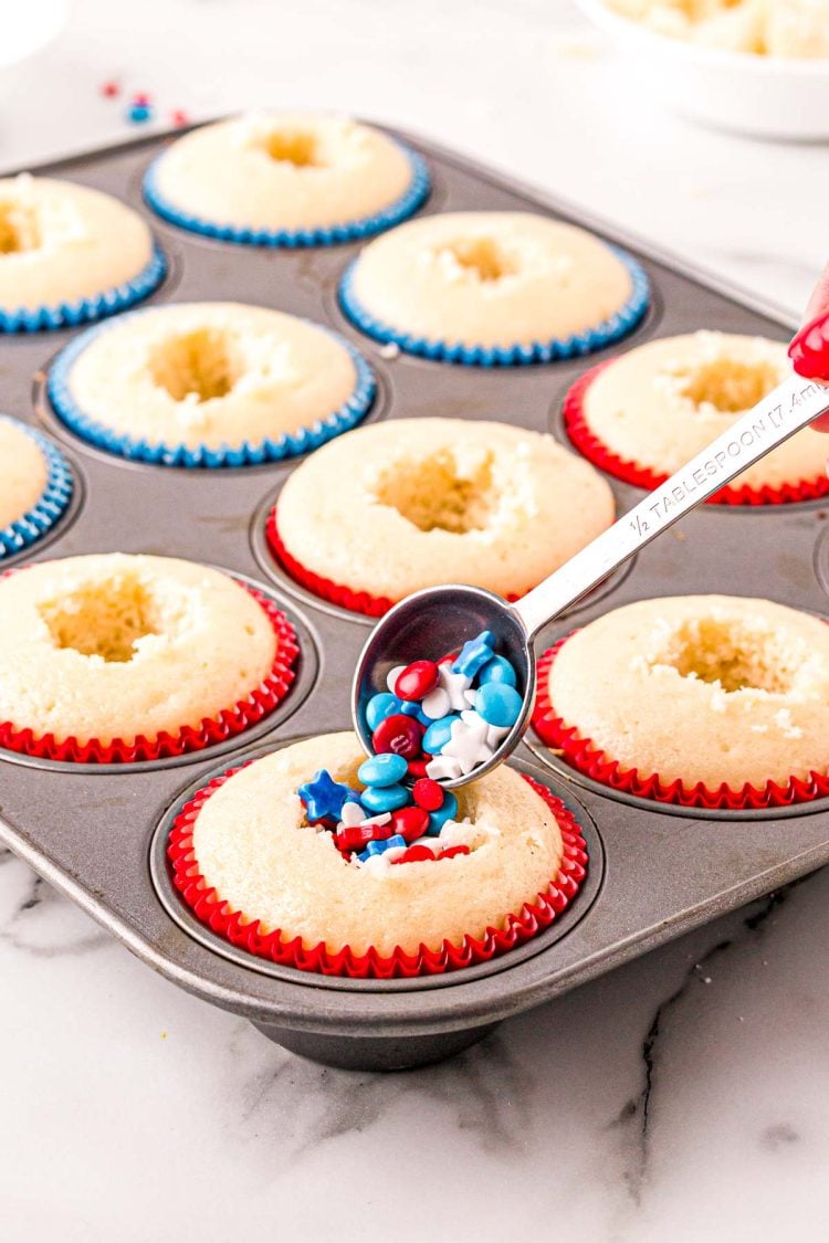 Red, white, and blue sprinkles being added to vanilla cupcakes.