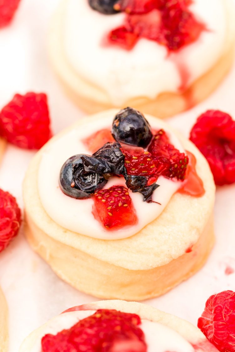 Close up photo of shortcake cookies topped with cream cheese frosting and berries.