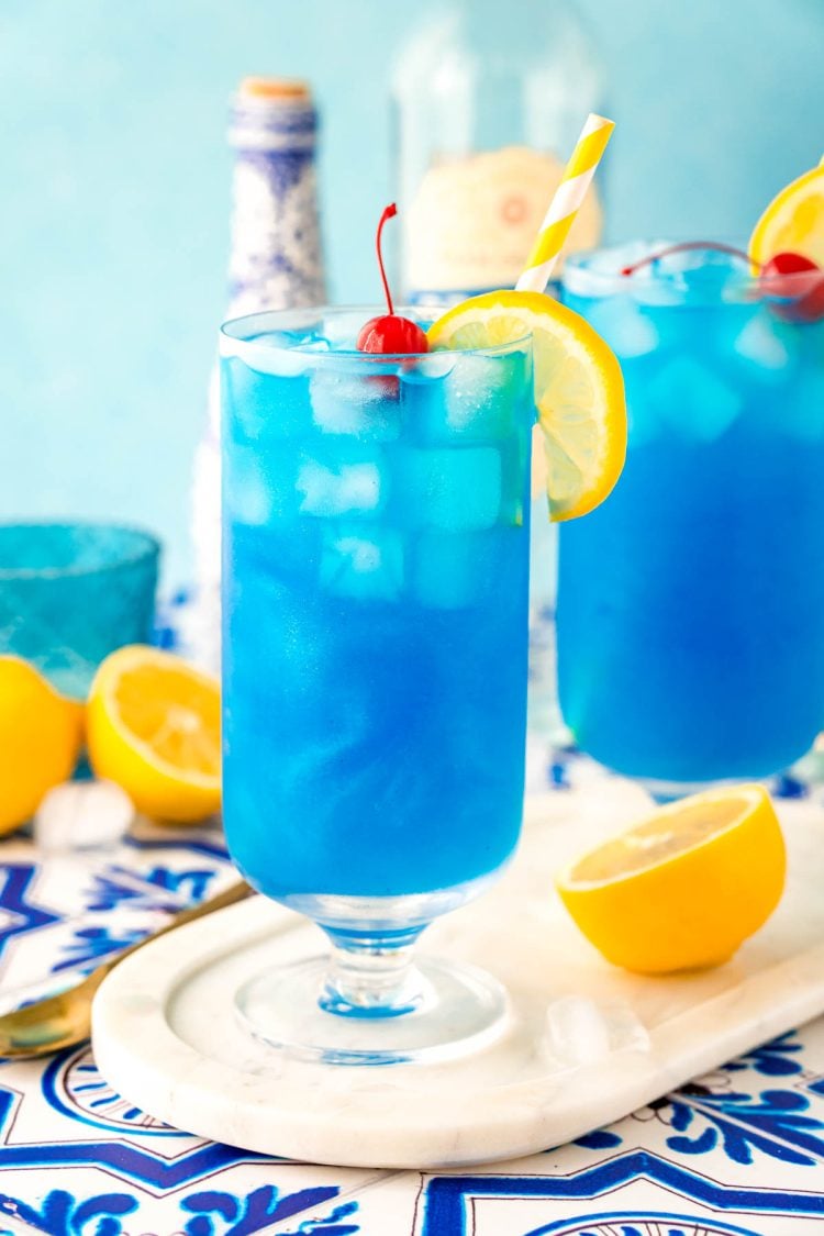 Blue lagoon cocktails in stemmed highball glasses on a white marble tray.