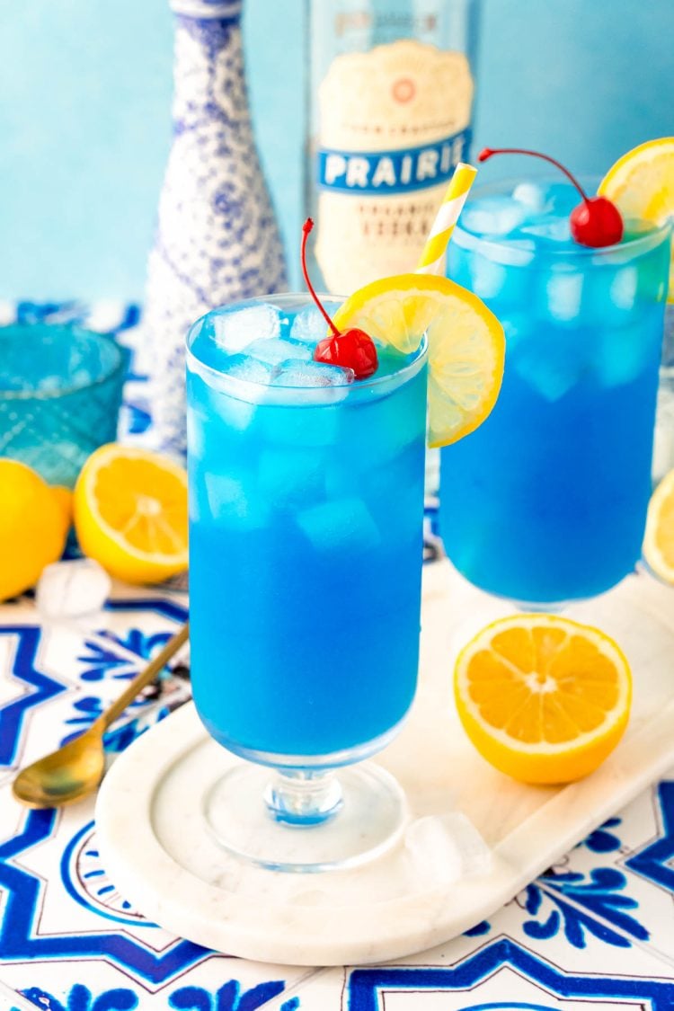 Blue lagoon cocktails in stemmed highball glasses on a white marble tray.