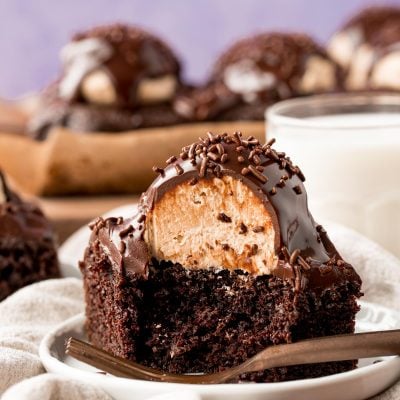 Close up photo of a slice of chocolate cake topped with a scoop of peanut butter frosting and topped with ganache.