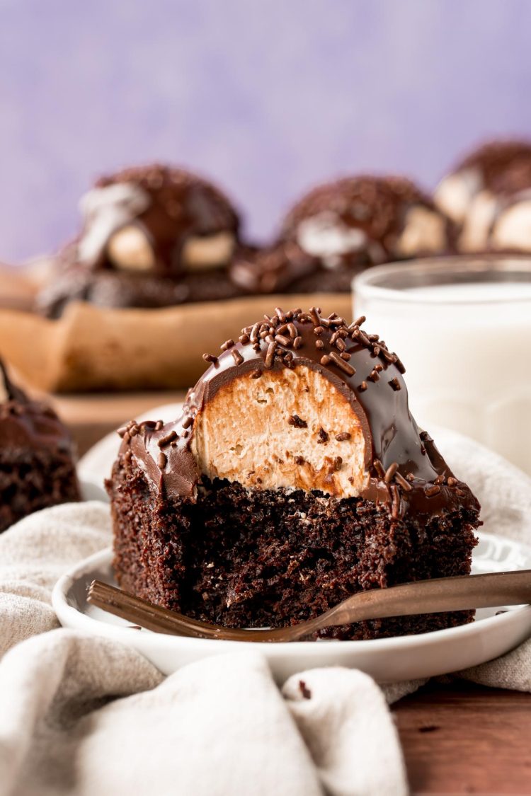 Close up photo of a slice of chocolate cake topped with a scoop of peanut butter frosting and topped with ganache.