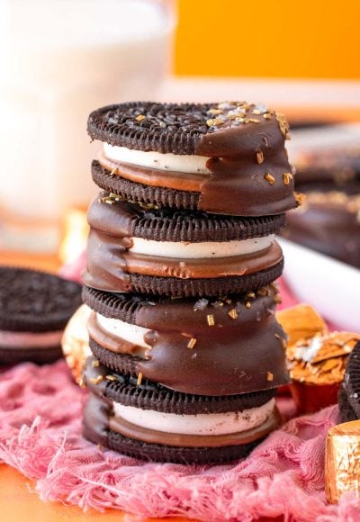 A stack of caramel chocolate dipped oreos on a pink napkin.