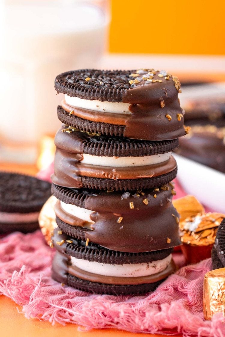 A stack of caramel chocolate dipped oreos on a pink napkin.