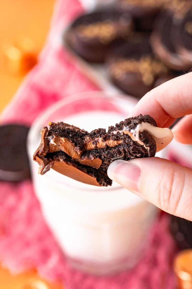 A woman's hand holding chocolate dipped oreos above a glass of milk.