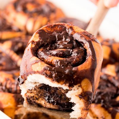 A spatula lifting a chocolate cinnamon roll out of the pan.