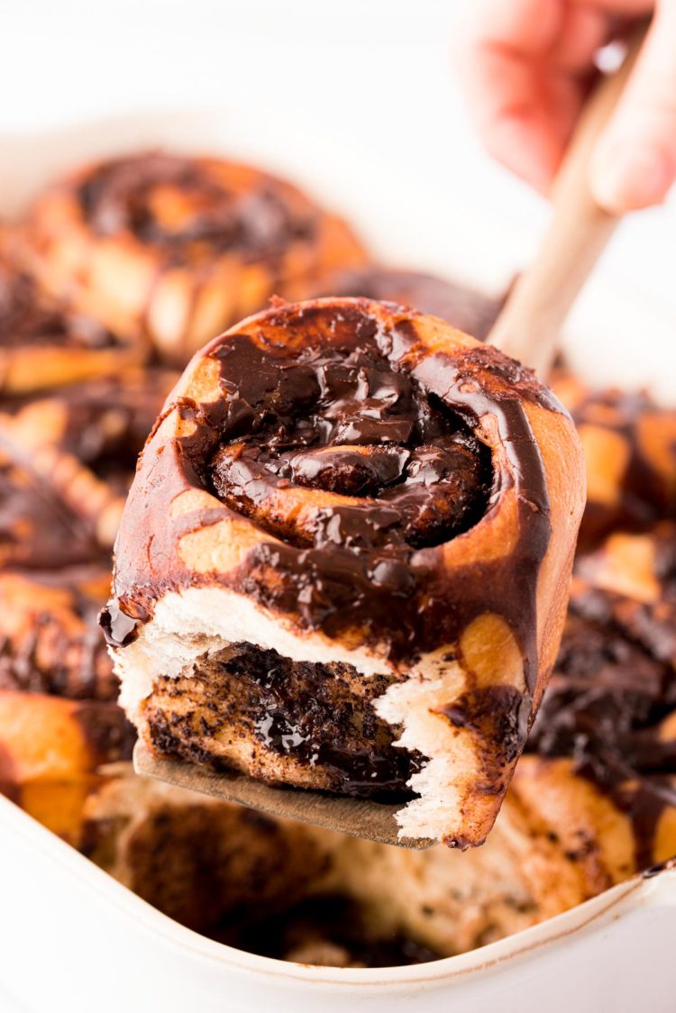 A spatula lifting a chocolate cinnamon roll out of the pan.