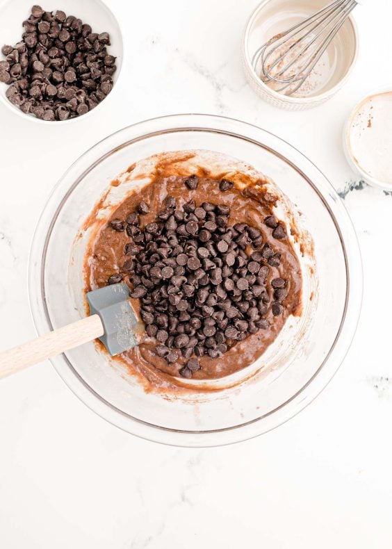 Chocolate chips being folded into a bowl of chocolate cake batter.