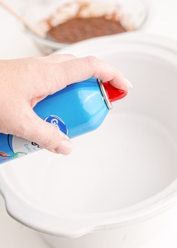 Nonstick spray being sprayed in a white crockpot.