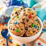 Close up of edible monster cookie dough in a white bowl on a blue and orange napkin.