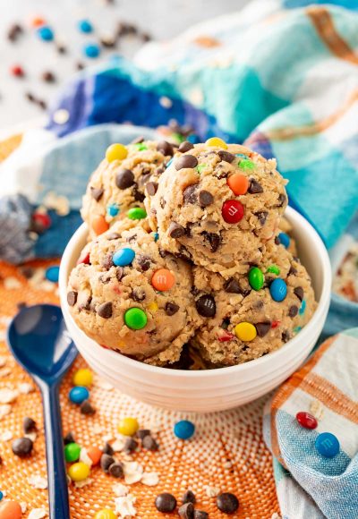 Close up of edible monster cookie dough in a white bowl on a blue and orange napkin.