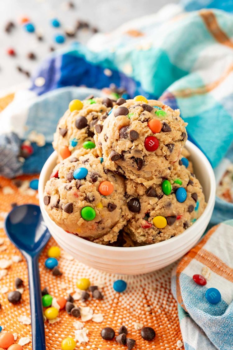 Close up of edible monster cookie dough in a white bowl on a blue and orange napkin.