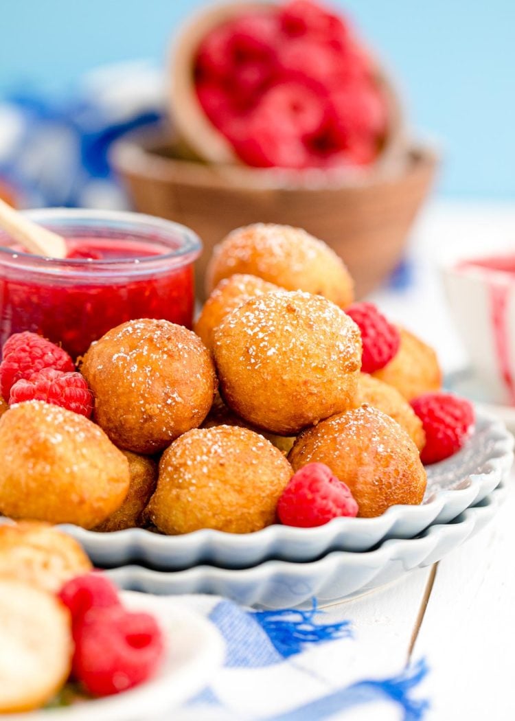 Close up photo of fried cheesecake on a scalloped plate with a jar of raspberry jam.