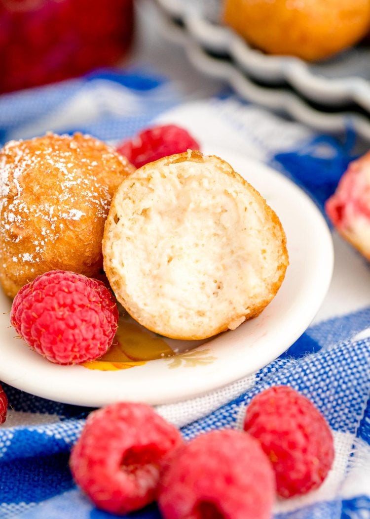 A fried cheesecake bite cut open on a white plate with raspberries around it.