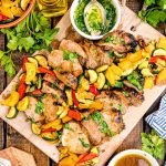 Overhead photo of pork tenderloin sliced on a wooden cutting board with vegetables.