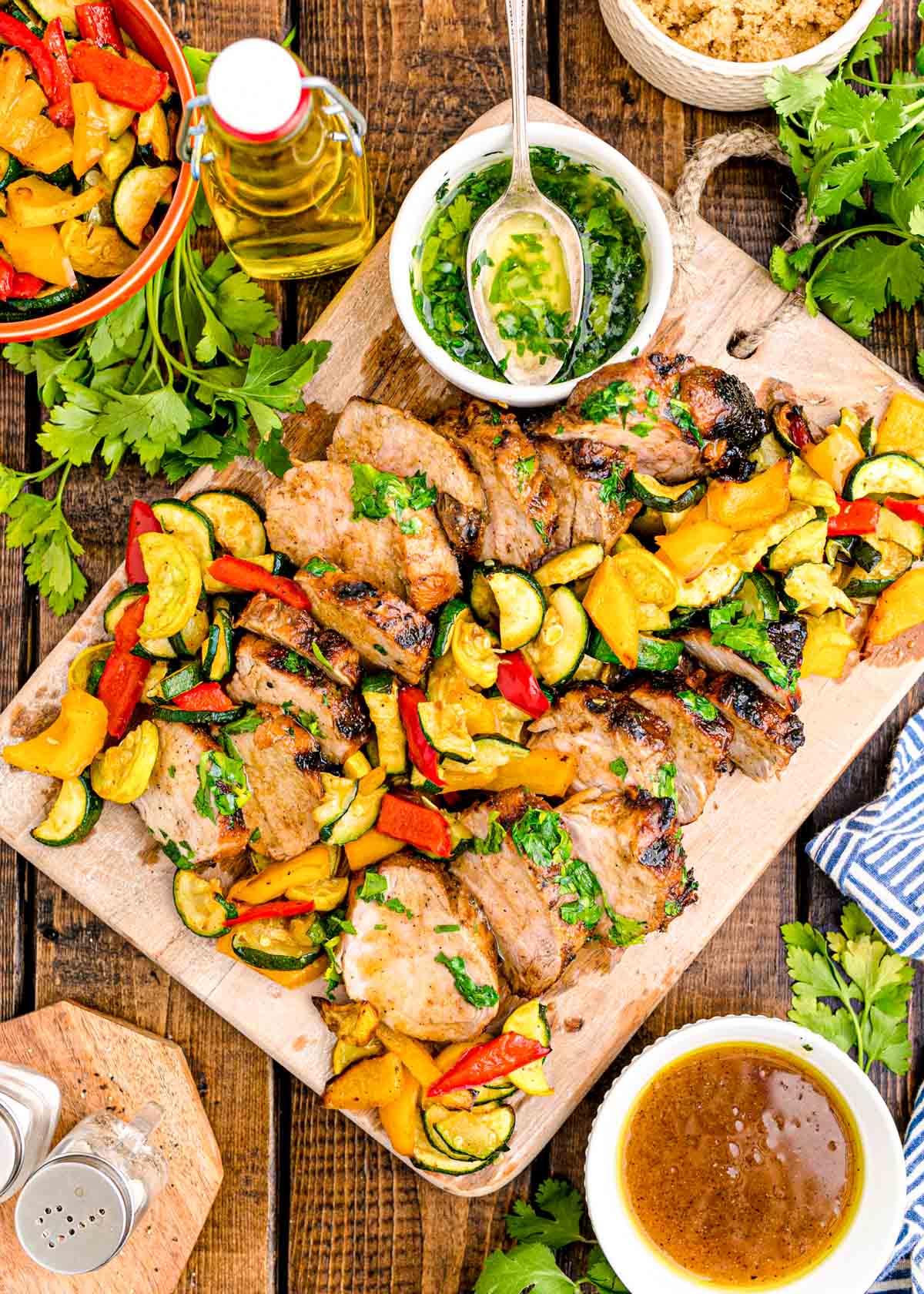 Overhead photo of pork tenderloin sliced on a wooden cutting board with vegetables.