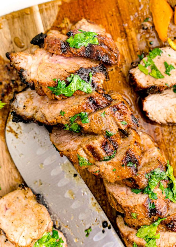 Pork tenderloin on a wooden cutting board sliced up.