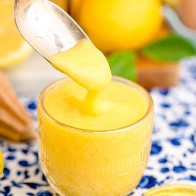 A spoon scooping lemon curd out of a glass dish.