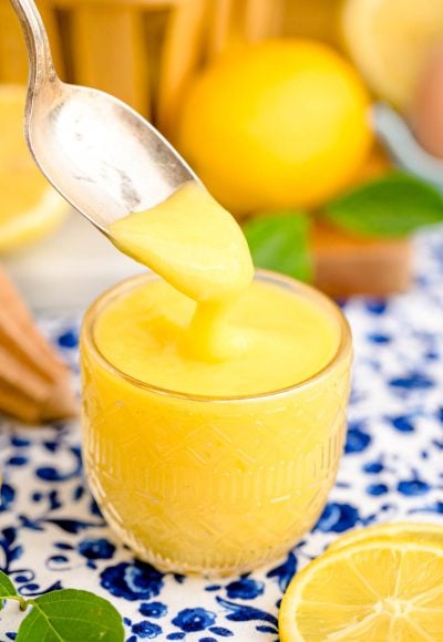 A spoon scooping lemon curd out of a glass dish.