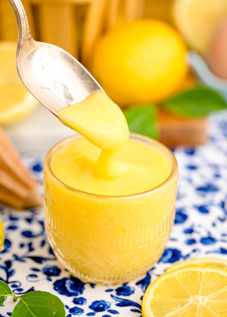 A spoon scooping lemon curd out of a glass dish.